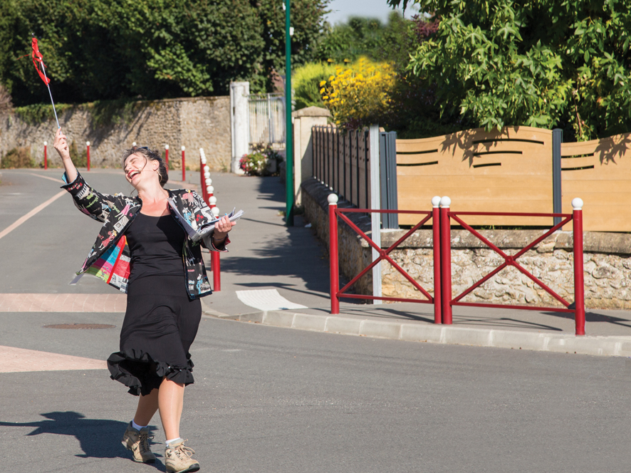 La visite Super guidée
Spectacle visite originale d'un bourg par Véronique Blot
crédit photo / Gérard Jégou Au milieu d'une rue, Véronique Blot incarne Sylvie Lamour la Super-guide touristique,
chaussures de randonnée aux pieds, jupe noire au vent, dans un élan en arrière, elle
éclate de rire et tend en l'air, à bout de bras, une baguette avec fanion rouge pour
que les touristes la repèrent dans le bourg et la suivent.